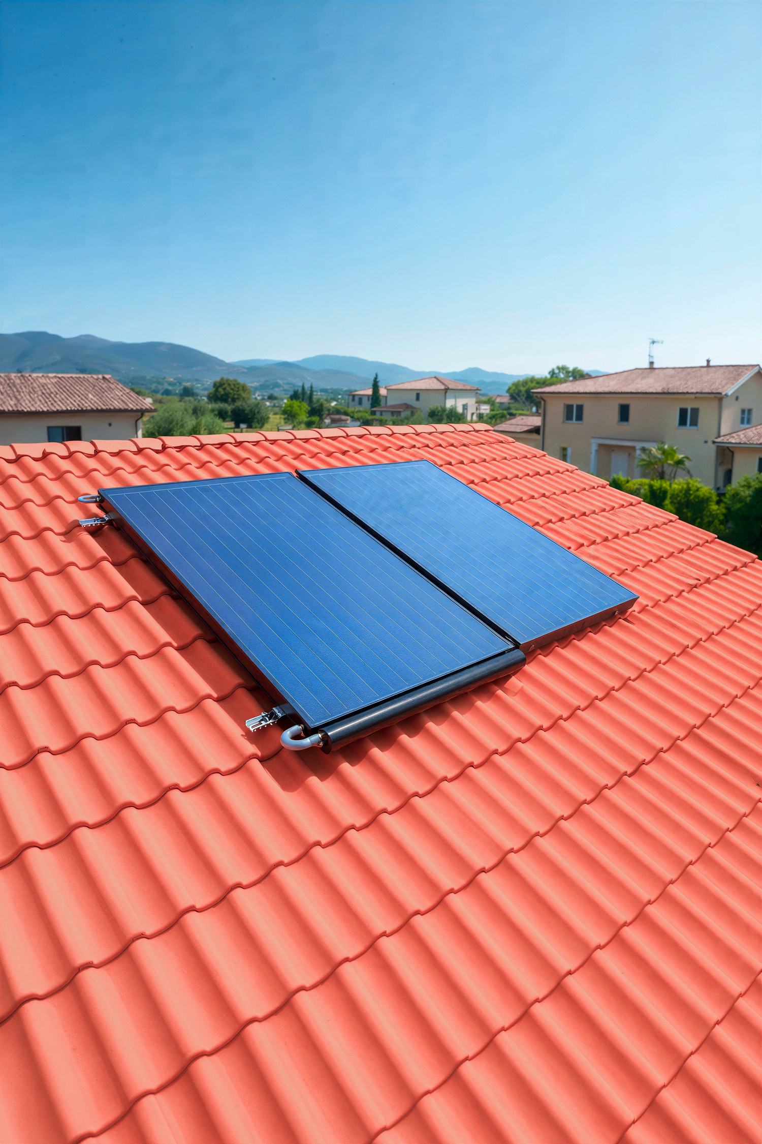 ELITE-TETTO - Pleion Solar panels mounted on a red tile roof under a clear blue sky with distant houses and hills in the background, indicating renewable energy.