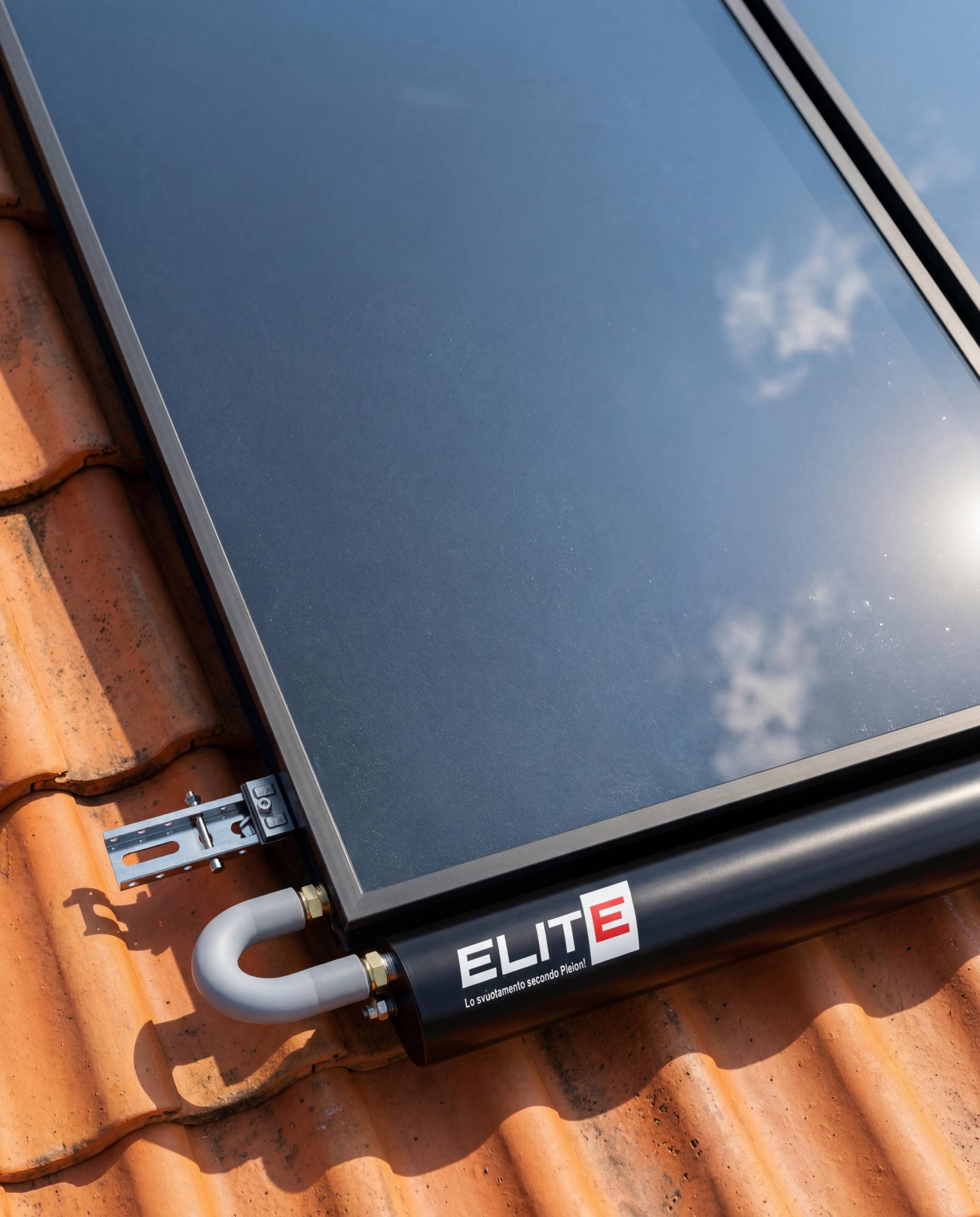 WhatsApp Image 2026-05-15 at 155639 - Pleion Close-up of a dark glazed panel mounted on orange clay roof tiles, with a metal bracket and a black ELITE device attached nearby.