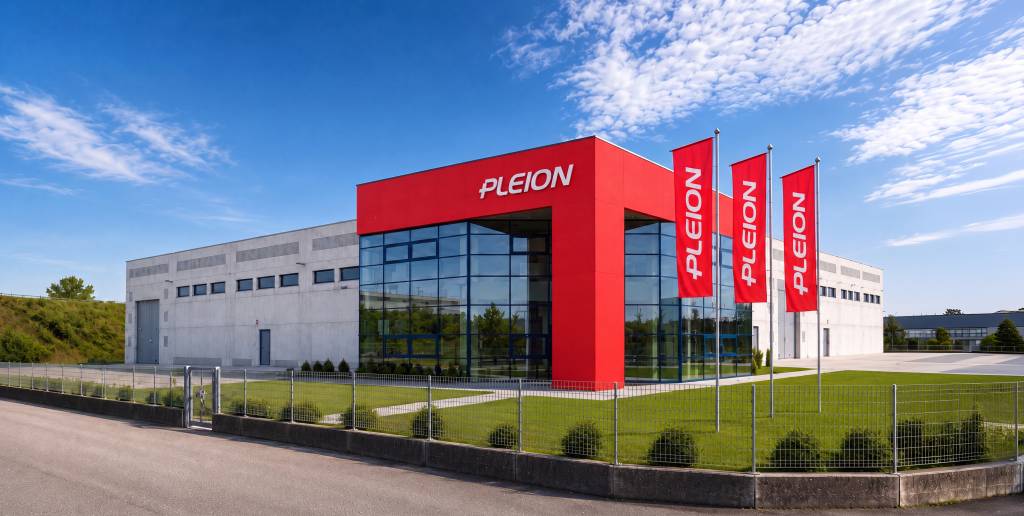 Immeuble de bureaux moderne doté d'une entrée d'un rouge vif et de quatre drapeaux rouges portant l'inscription « PLEION » sous un ciel bleu.