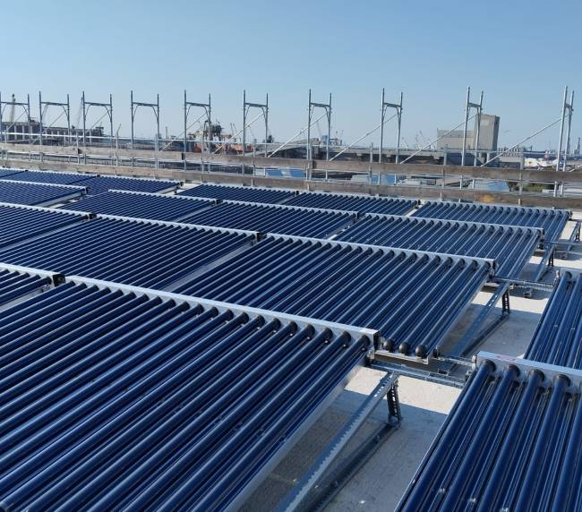 Rows of blue evacuated-tube solar collectors on a rooftop against a clear blue sky.