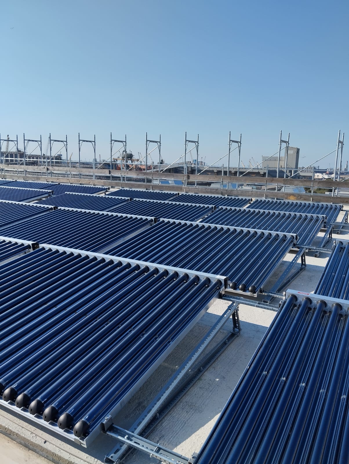 Rows of blue evacuated-tube solar collectors on a rooftop against a clear blue sky.