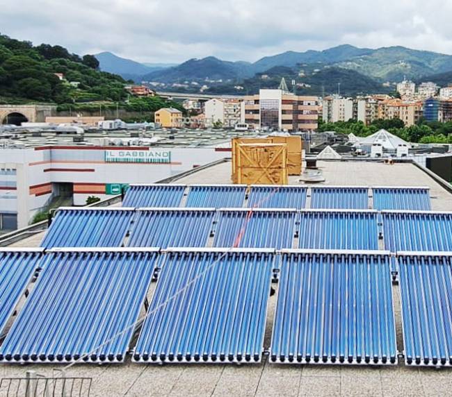 Rooftop solar panels in neat rows overlook a city with green hills under a cloudy sky.