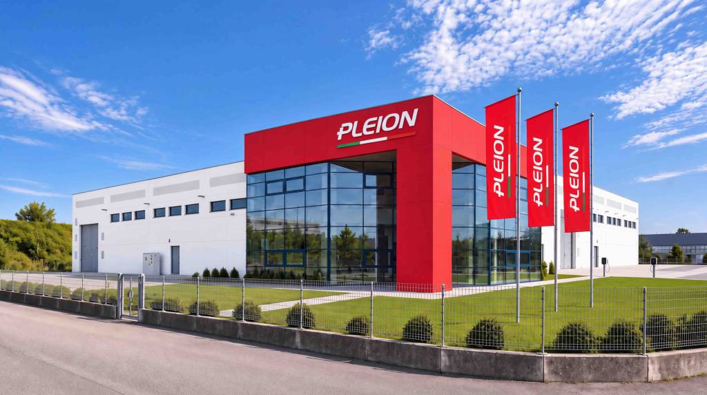 Modern commercial building with a red entrance and four tall red Pleion flags in front under a blue sky.